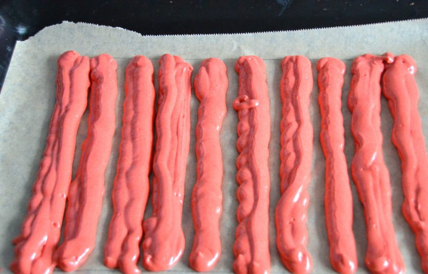 1. Этап. Пирожное Красное и белое: Подготовьте 2 листа пергамента, для выпечки двух коржей. На оборотной стороне пергамента нарисуйте контур размером с лист формата А4. Разделите тесто на 2 части. Переложите тесто (примерно 340 грамм) в одноразовый кондитерский мешок и нанесите толстые полоски на контур, обозначенный на пергаменте.