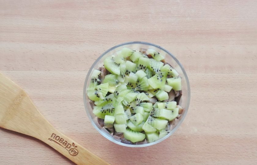 1. Этап. Салат с курицей, киви и грибами: Киви помойте, очистите и нарежьте небольшими кубиками. Это будет следующий слой салата. Покройте его майонезом.