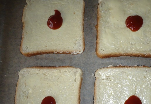 1. Этап. Горячие сэндвичи с фаршем индейки: Противень застелите пергаментной бумагой и выложите 4 ломтика тостового хлеба. Ломтики хлеба смазать сливочным маслом, сверху масла смазать кетчупом.