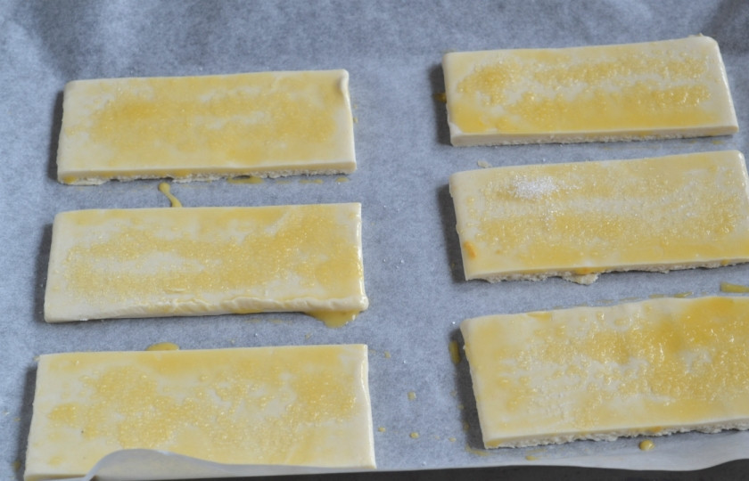 1. Этап. Язычки из готового слоеного теста: Смажьте каждый кусочек яйцом и присыпьте небольшим количеством сахара.