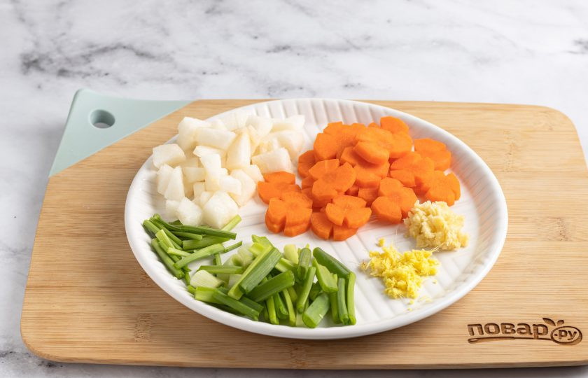 1. Этап. Набак кимчи на воде: Порежьте морковь кружочками. Можно придать моркови форму цветочка, если сделать ножом 3-4 продольных бороздки длинною 2-3 мм. Стебли петрушки и зеленый лук порежьте на равные части примерно по 3-4 см. Грушу очистите от кожуры, удалите сердцевину и порежьте на тонкие квадратики. Корень имбиря и чеснок мелко измельчите, либо нарежьте тонкими ломтиками. Все подготовленные ингредиенты добавьте к китайской капусте с дайконом. Перемешайте.