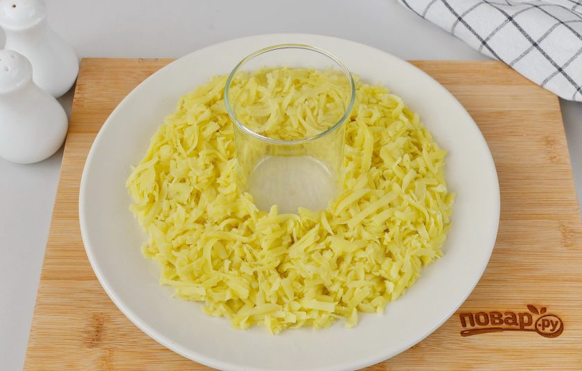 1. Этап. Салат Гранатовый браслет с курицей и яблоком: Возьмите большое блюдо для салата, в центр поставьте стаканчик. Вокруг распределите тертый картофель. Посолите немного.