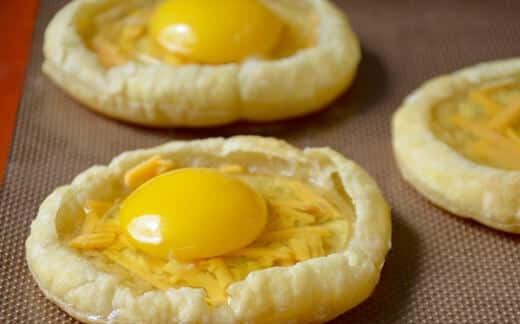 1. Этап. Яичница на слоеном тесте: 3. Достаньте тесто и сразу отправьте в разогретый до 200 градусов духовой шкаф на 8 минут, затем удалите формы из печи и в центр каждой насыпьте немного тертого сыра и вбейте по одному яйцу, посолите.