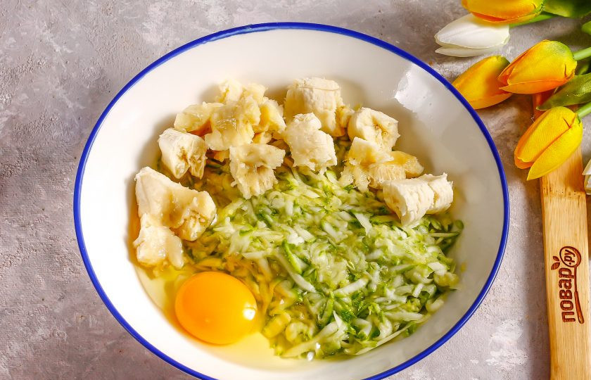 1. Этап. Оладьи из кабачков с бананом: Очистите банан от кожуры и разломите на кусочки, добавьте в емкость. Вбейте туда же куриное яйцо. Всыпьте сахар и тщательно все перемешайте, пюрируя кусочки банана.