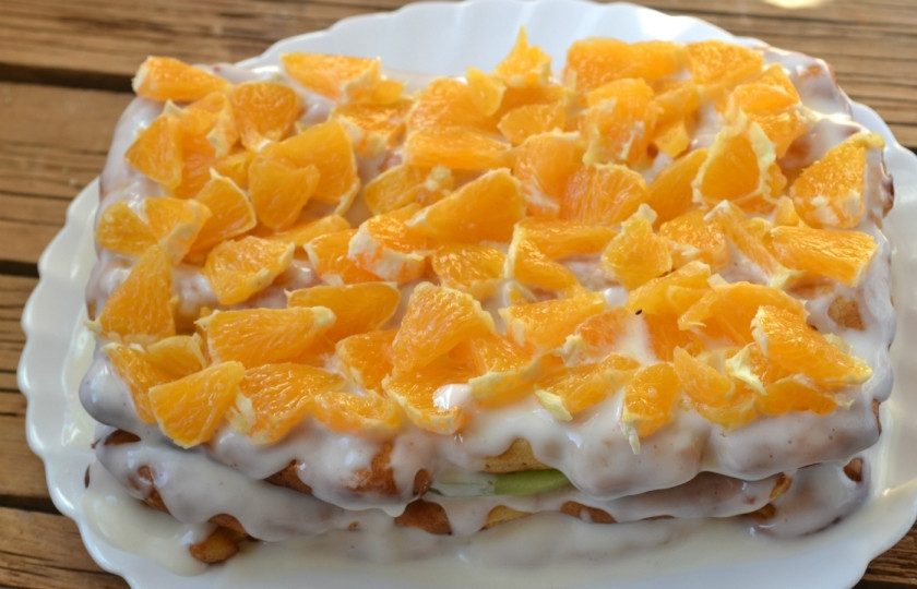 1. Этап. Торт из заварного теста с фруктами: Положите сверху третий корж, залейте торт остатками крема так, чтобы тот покрывал торт и сверху, и по бокам. Украсьте торт измельченным апельсином. Отправьте его в холодильник минимум на 2 часа, чтобы он пропитался и стал 
