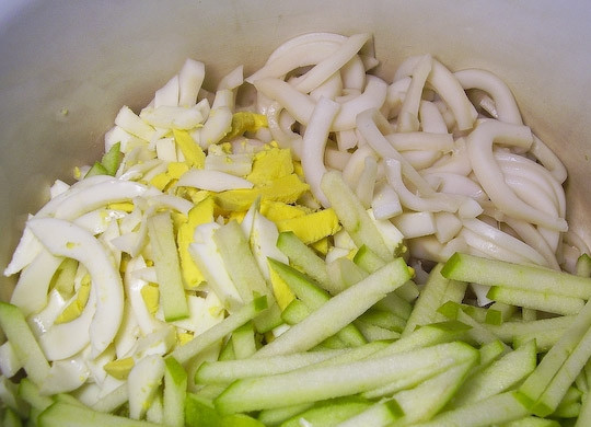 1. Этап. Салат из кальмаров с кукурузой: Очистите яблоко, удалите из него сердцевину с косточками. Огурец вымойте, снимите с него кожуру. Яйца отварите вкрутую и очистите от скорлупы. Все ингредиенты нарежьте соломкой и положите в миску. Посолите и заправьте майонезом.