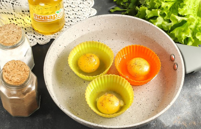1. Этап. Яйцо пашот в силиконовой форме: Посолите и поперчите яйца. Выложите формочки в сковороду или широкий ковш. Влейте теплую воду до середины формочек в емкость и поместите ее на плиту. Включите умеренный (средний) нагрев.
