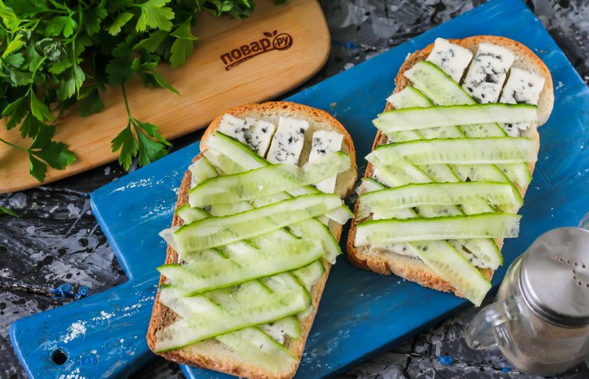 1. Этап. Мини-пицца Мумия: Огурец небольшого размера промойте в воде, срежьте с него хвостики и обязательно попробуйте на вкус, чтобы он не был горьким. Нарежьте с помощью овощечистки тонкими лентами. Выложите ленты на слой сыра по диагонали сначала в одну сторону, затем в другую. Сверху оставьте немного места для глаз. Разогрейте духовку, поместите в нее подготовленные мини-пиццы на 5 минут до расплавления сырного слоя.