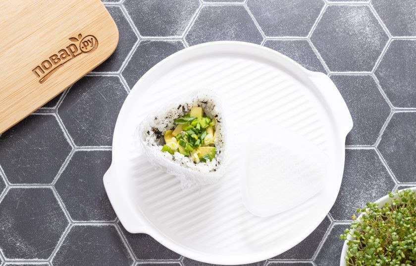 1. Этап. Яки онигири: Положите примерно 1 ст.л. риса в форму для онигири и слегка расплющьте ее, сделайте небольшое углубление. Сверху выложите немного начинки из творожного сыра, авокадо и зеленого лука.