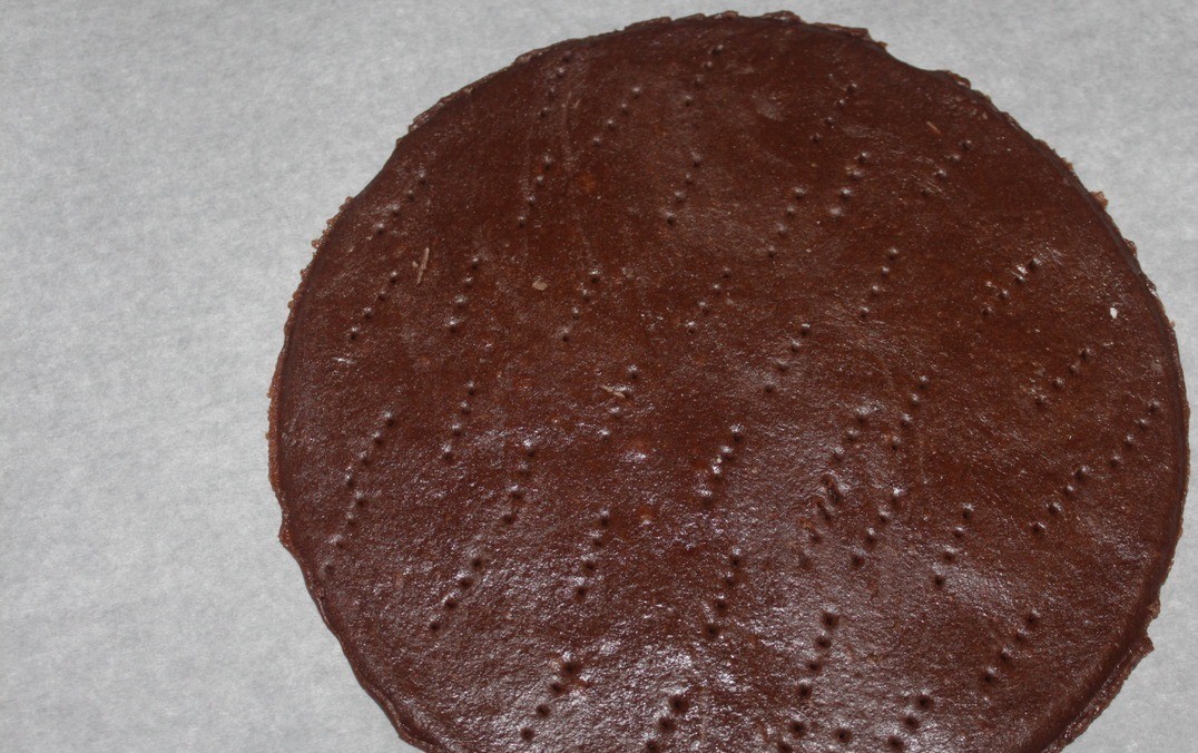 1. Этап. Торт Медовик шоколадный: После истечения времени даем тесту остыть немного. Замешиваем гладкое блестящее тесто при помощи 1-2 ст. л. муки. Тесто не должно липнуть к рабочей поверхности и рукам. Делим его на 4 части. Разогреваем духовку до 180 градусов. Раскатываем каждую часть теста сразу на пергаменте в тонкий пласт 2-3 мм. С помощью бортика формы d 20 см для выпекания вырезаем круг, обрезки оставляем. Накалываем корж часто вилкой и печем в течение 4-5 минут.