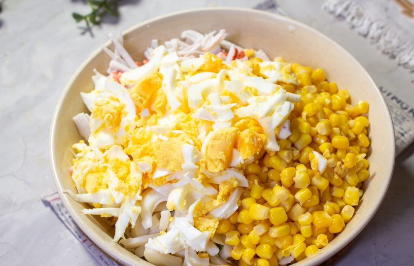 1. Этап. Салат с крабовыми палочками, кальмарами и кукурузой: Куриные яйца отварите вкрутую, остудите и очистите. Нарежьте яйца тонкой соломкой и отправьте в салатник.