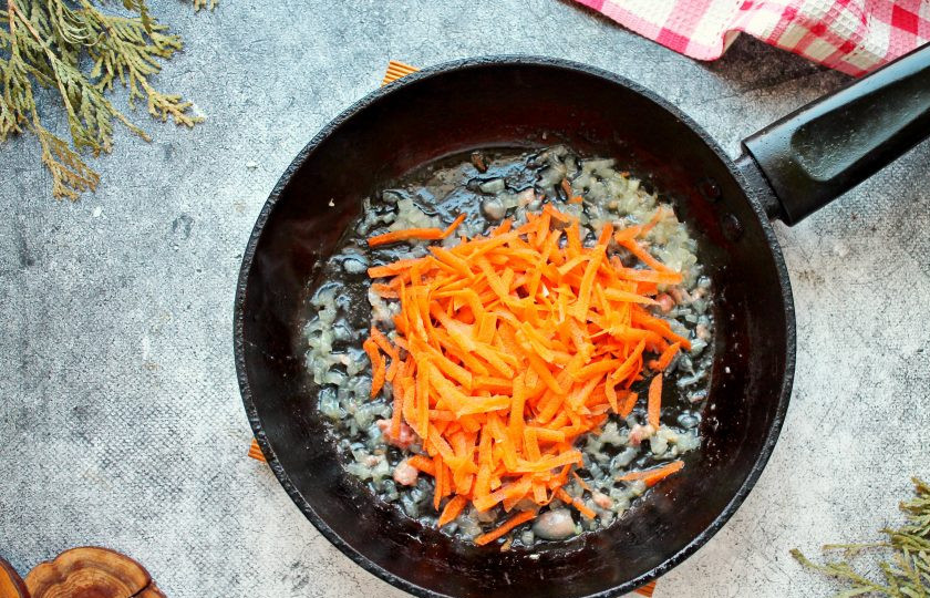 1. Этап. Кукурузная каша с тушенкой: Морковь натрите на крупной терке и добавьте в сковороду. Обжаривайте овощи еще 3-4 минуты, перемешивая.