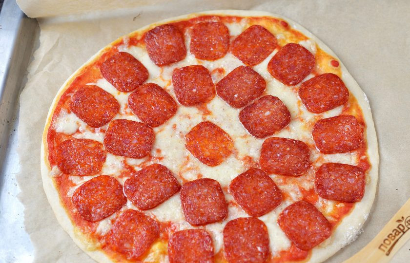 1. Этап. Пицца Дьявола: Колбасу нарежьте тоненькими слайсами. Извлеките готовую пиццу из духовки, быстро выложите поверху пепперони и дайте минут 5 постоять. За это время колбаса прогреется и из нее немного выделится жир.