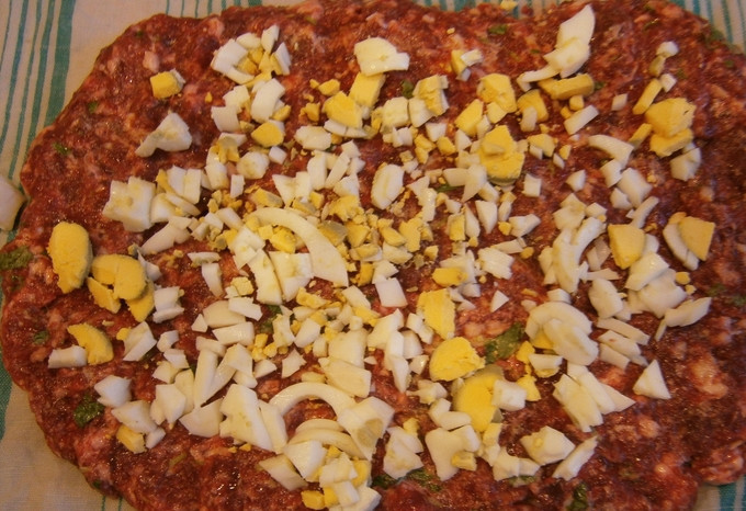 1. Этап. Мясной рулет из лосятины: Смочите чистое полотенце водой. Аккуратно выложите на него фарш, разровняйте его мокрыми руками. Вареное яйцо измельчите и распределите по фаршу.