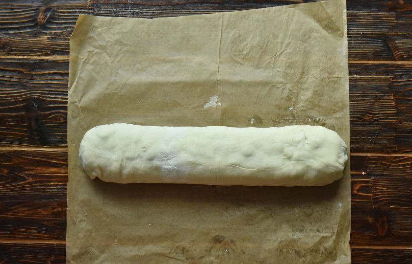 1. Этап. Штрудель с вишневой начинкой классический: Закрепите шов и тесто по краям штруделя. Выложите изделие швом вниз и перенесите вместе с бумагой на противень. Пергаментную бумагу слегка смочите водой с помощью кулинарной кисти.