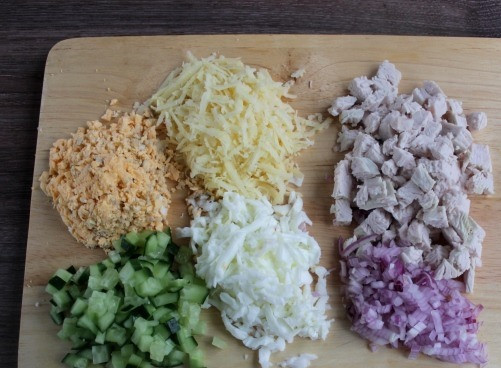 1. Этап. Новогодний салат Символ года: Сыр натереть на терке, у яиц отделить белок и желток и тоже натереть на терке. Лук нарезать на мелкие кубики, облить холодной водой, обсушить на бумажном полотенце. Филе индейки нарезать небольшими кубиками. 1 огурец нарезать кубиками.