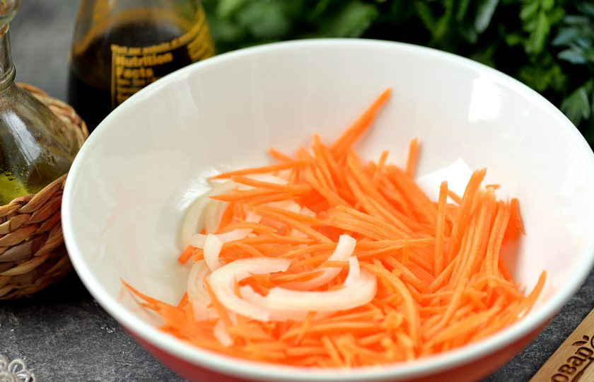 1. Этап. Холодная закуска из куриных сердечек в чесночно-соевом соусе: Репчатый лук нарежьте полукольцами, морковь натрите тонкой соломкой, выложите овощи в глубокую миску.
