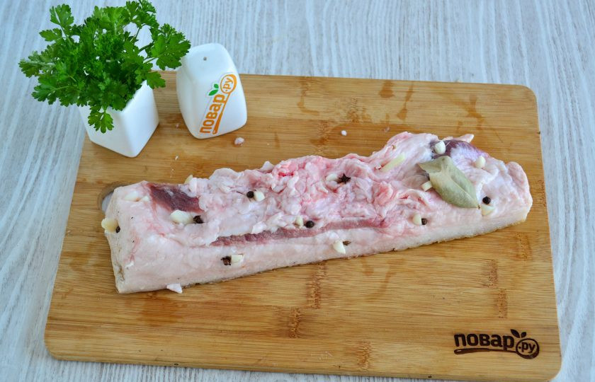 1. Этап. Сало в рукаве в духовке: Чеснок порежьте на продолговатые кусочки. В сале по всему куску сделайте надрезы и вставьте в них кусочки чеснока, перец горошком и гвоздику.