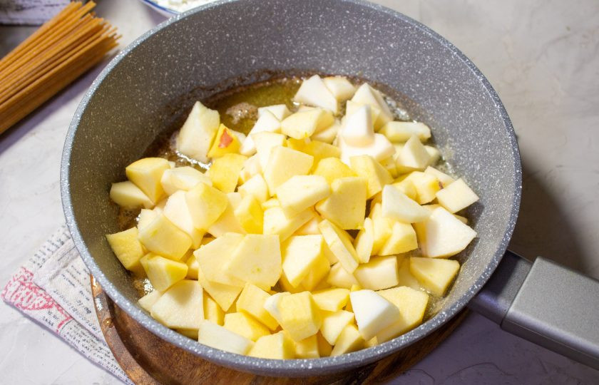 1. Этап. Спагетти с творогом и яблоком: Яблоки очистите от кожуры и удалите семенную коробку. Мякоть яблок нарежьте небольшим кубиком, отправьте в сковороду и готовите, помешивая минут 5-7, до их мягкости.