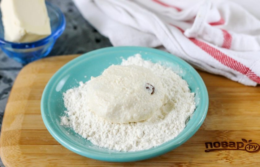 1. Этап. Сырники из кислого творога: Оставшуюся муку высыпьте на блюдце. Смочите руки в воде, сформируйте из части творожного теста округлую заготовку, обпанируйте ее со всех сторон в муке.