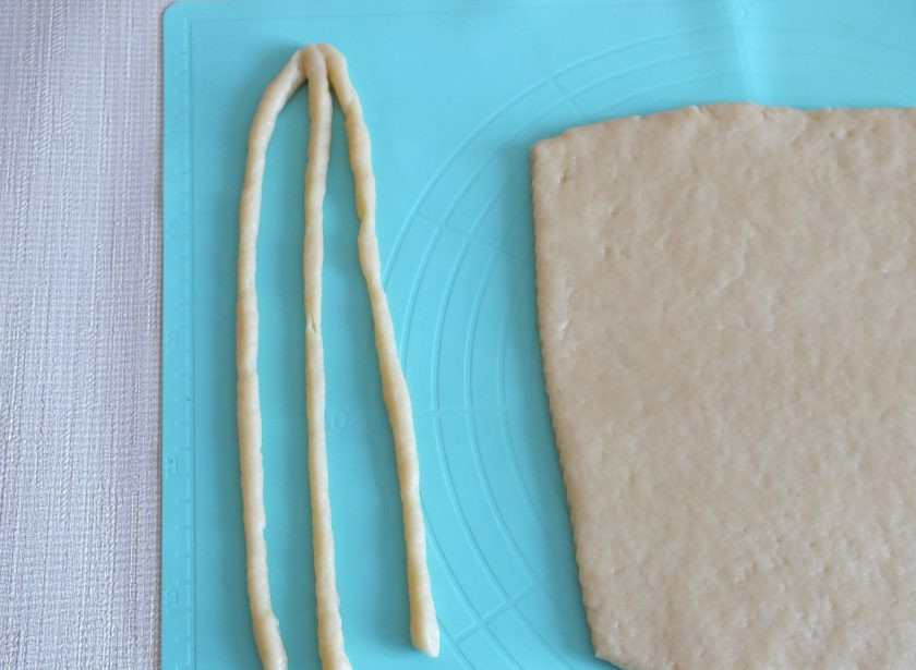 1. Этап. Печенье Косичка: Тесто раскатайте пласт толщиной 0,5 см. Нарежьте на тонкие полоски длиной 20 см. Соедините по три штучки и заплетите длинную косичку.