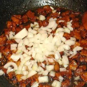 1. Этап. Жареная колбаса с картофелем: Добавляем кусочки бекона. Обжариваем, добавляем лук и чеснок.