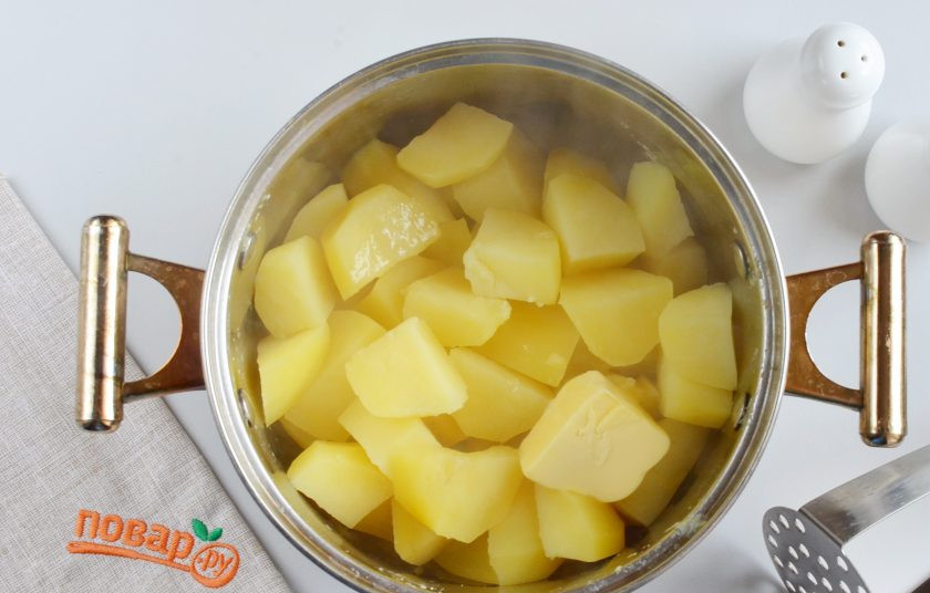 1. Этап. Фаршированные картофельные оладьи: С картофеля слейте всю воду, выложите кусочек масла и толкушкой превратите в пюре. Совет! Не стоит пользоваться блендером, иначе картофель станет очень вязким и для рецепта не подойдет.