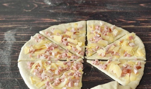 1. Этап. Рогалики с копчёной грудинкой и сыром: Разрежьте пласт теста на 8 сегментов и сверните каждый в рогалик.