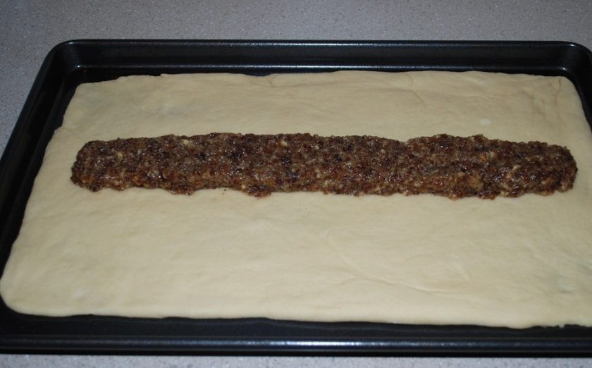 1. Этап. Плетенка с черносливом: 3. В отдельной миске смешайте измельченный чернослив и грецкие орехи, цедру, мускатный орех, 2 столовые ложки сливочного масла и 2 столовые ложки сахара. Разместите тесто на противень для выпекания и в середину вдоль положите приготовленную начинку из чернослива.