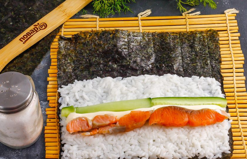 1. Этап. Темпура роллы: На рис выложите сливочный сыр и ломтики слабосоленой семги или лосося. Нарежьте промытый огурец длинными ломтиками и добавьте к остальной начинке.
