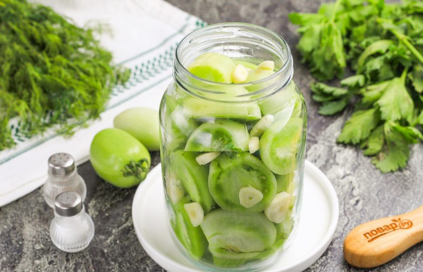 1. Этап. Как зеленые помидоры засолить на зиму в банках: Выложите помидоры в банку или пищевой контейнер, в котором будете солить их. Нарежьте чесночные зубчики ломтиками и всыпьте их туда же.