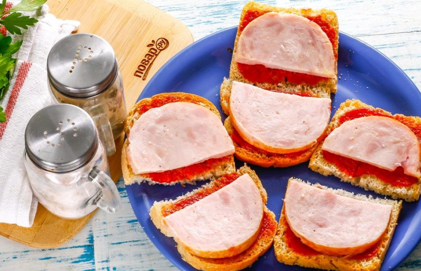 1. Этап. Бутерброды с ветчиной и сыром: Ветчину нарежьте кружочками, а кружочки - разрежьте пополам и выложите на слой кетчупа. Вместо ветчины можно использовать копченое мясо, колбасу: копченую или вареную.