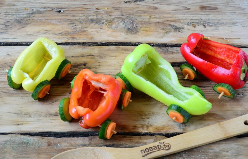 1. Этап. Нарезка Овощной поезд: Сладкий перец очистите, но не так, как вы привыкли это делать. Положите перчинку на рабочую поверхность и вырежьте прямоугольник. Выньте семечки и перепонки, а затем промойте. Вагончики почти готовы, осталось сделать колеса. В этом деле нам поможет огурец и морковь. Оба эти овоща порежьте на кружочки толщиной 3 мм. При помощи зубочисток или бамбуковых шпажек прикрепите колеса из огурцов и помидоров, как показано на фото. Вот наши вагончики и готовы.
