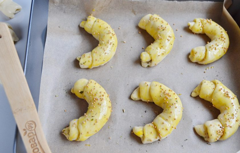 1. Этап. Круассаны-рогалики с прованскими травами: На пергамент уложите рогалики на расстоянии друг от друга. Смажьте желтком, посыпьте морской солью, прованскими травами, зернами горчицы.