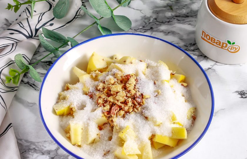 1. Этап. Рулет с яблоком и орехами: Яблоки промойте в воде, разрежьте на четыре части и срежьте семенные блоки. Нарежьте мелкими или средними кубиками и высыпьте нарезку в глубокую емкость. Протрите в руках ядра грецких орехов, добавьте в емкость вместе с сахаром. Перемешайте.