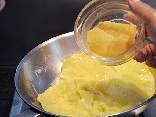 1. Этап. Омлет кусочками: 4. Дайте яйцам немного поджариться, добавьте на сковороду сыр. Его можно выложить небольшими кубиками, а можно предварительно натереть на терке. При помощи лопатки начните аккуратно все перемешивать.