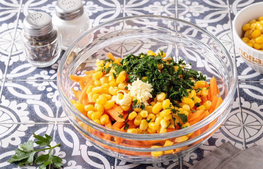 1. Этап. Салат с морковью, огурцом и кукурузой: Петрушку мелко порубите, чеснок пропустите через пресс, добавьте к остальным ингредиентам.
