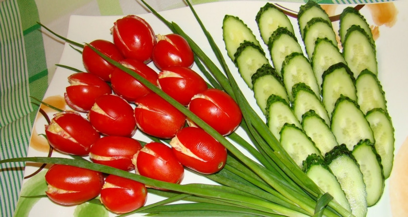 1. Этап. Салат к 8 марта: 4. Выкладываем начиненные помидоры на блюдо, украшаем зеленью и огурчиками. Помидоры будут напоминать бутоны, зеленый лук стебли, а огурцы - листочки. Вот такое красивое блюдо сможет украсить ваш праздничный стол.