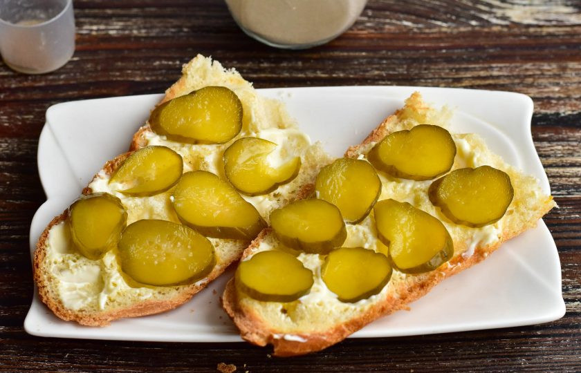 1. Этап. Голландские бутерброды с селедкой на багете: Смажьте майонезом и выложите соленый огурец, который нарежьте тонкими кружочками.