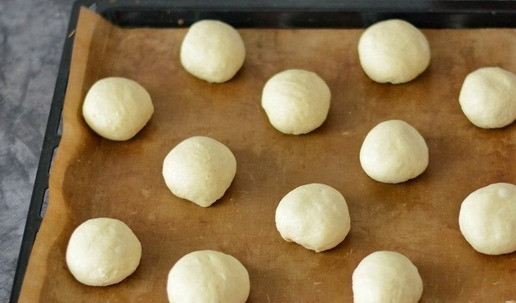 1. Этап. Булочки сахарные из ночного теста: Согревшееся тесто ещё раз вымесите на столе и разделите на небольшие булочки. Булочкам придайте круглую форму, скатав их в шарики. Выложите булочки на противень, застеленный пергаментом.