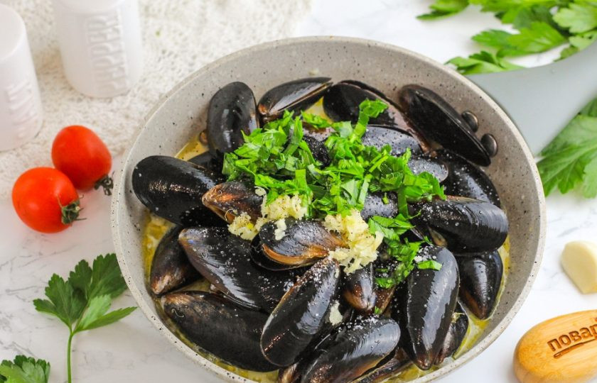 1. Этап. Мидии в сливочно-чесночном соусе: Промойте и измельчите зелень петрушки, кинзы или укропа. Добавьте ее в емкость и перемешайте. Прикройте сковороду крышкой, но не накрывайте полностью.