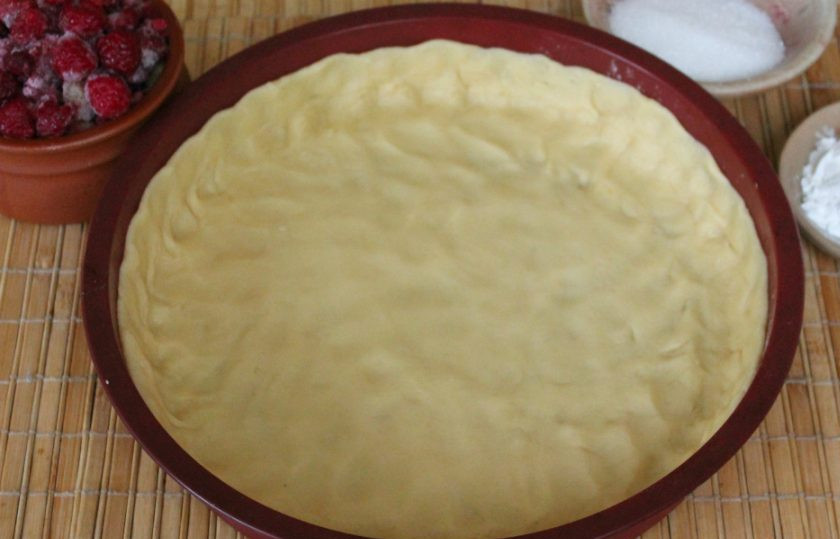 1. Этап. Песочный пирог с малиной: Тесто перекладываем в силиконовую форму и распределяем по дну. По периметру оставляем бортик. Пальцы нужно посыпать мукой, чтобы тесто не прилипало.