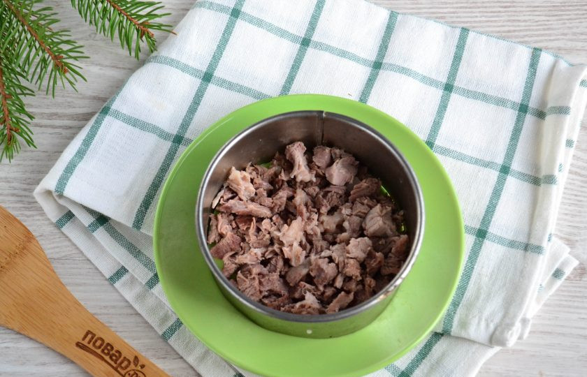 1. Этап. Мясной салат с орехами: Половину отваренной свинины мелко нарежьте. Оформлять салат можно просто слоями или с помощью сервировочного кольца. Выложите мясо первым слоем. Покройте сеточной майонеза.