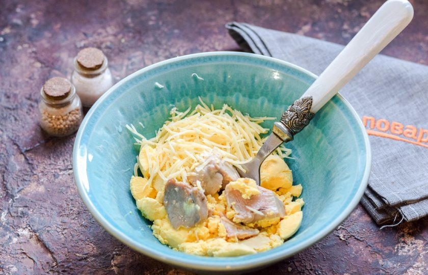 1. Этап. Фаршированные яйца на год Быка: Куриные желтки переложите в миску, добавьте печень трески. Твердый сыр натрите на мелкой терке, добавьте в миску к желткам и печени.