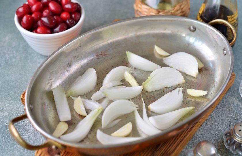 1. Этап. Курица с кизилом в духовке: Нарежьте лук дольками, чеснок можно положить целыми зубчиками или порезать пластинками, выложите их на дно формы, в которой будете запекать курицу.