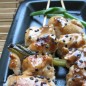 Якитори Нарезать филе (вкуснее, если брать мясо с бедра, я использовала грудку) кусочками со стороной 3 см. Измельчить чеснок, натереть имбирь. Влить в сотейник соевый соус, вино, кунжутное масло, всыпать сахар, красный перец, добавить чеснок и имбирь. Довести до кипения и кипятить на слабом огне около 10-15 минут – соус должен густеть. Как вариант – добавить к холодным ингредиентам дополнительно 1 ст. л. муки. Тогда смесь загустится через минуту. При варке помешивать! Во время варки якитори-соуса вы занимаетесь шпажками. Вы можете просто нанизать цыпленка на палочки, смазать соусом и жарить – будет очень вкусно, а можете, как и я, добавить зеленого цвета и сделать интересную сдвоенную форму. Для сдвоенного якитори используйте молодой порей или зеленый лук потолще. Отрезаем кусок белой и кусок зеленой части – оставляем толстую белую часть и немного зеленых побегов. Нанизывайте кусочек мяса, перемежая его луковым столбиком таким образом, чтобы этот столбик был общим на 2 шпажки. У меня вышло по 3 кусочка на шпажке и 2 общих стебля лука. Соус разделить на 2 части – для смазывания при запекании и для подачи. Смажьте кисточкой с соусом наши заготовки с одной стороны. Разогрейте сковороду-гриль или воспользуйтесь духовкой с решеткой для запекания. Смажьте гриль. Зажаривать начинайте с маринадной стороны, немного придавливая шашлычки при жарке. Смажьте вторую сторону соусом с процессе. Переверните. Гриллование должно продолжаться минут 5-7, а то мясо может стать сухим. Положить на блюдо, смазать оставленным в другой чашке соусом (он станет за это время более густым и более темным). По желанию посыпать кунжутом.