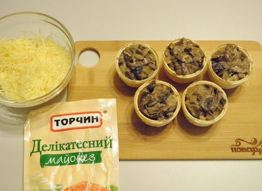 1. Этап. Тарталетки с грибами: Чуть остывшие грибы разложите по тарталеткам, приготовьте тертый сыр и майонез.