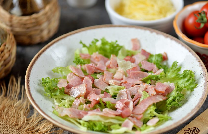 1. Этап. Салат Фризе с беконом: Выложите салатные листья в тарелку, посыпьте их слегка остывшим беконом.