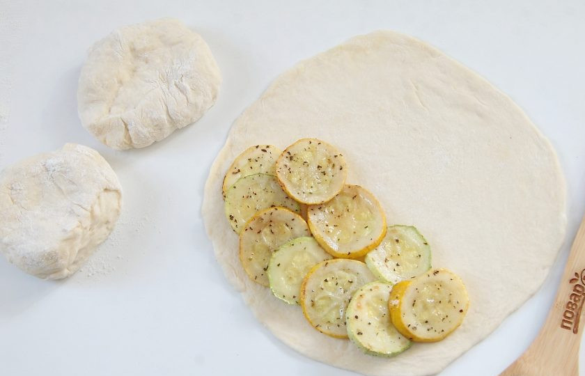1. Этап. Кальцоне с цукини, оливками и моцареллой: Подошедшее тесто разделите на три части. Раскатайте поочередно каждую часть в форме круга, диаметром не более 20 см и выложите на одну половину несколько кружков цукини.