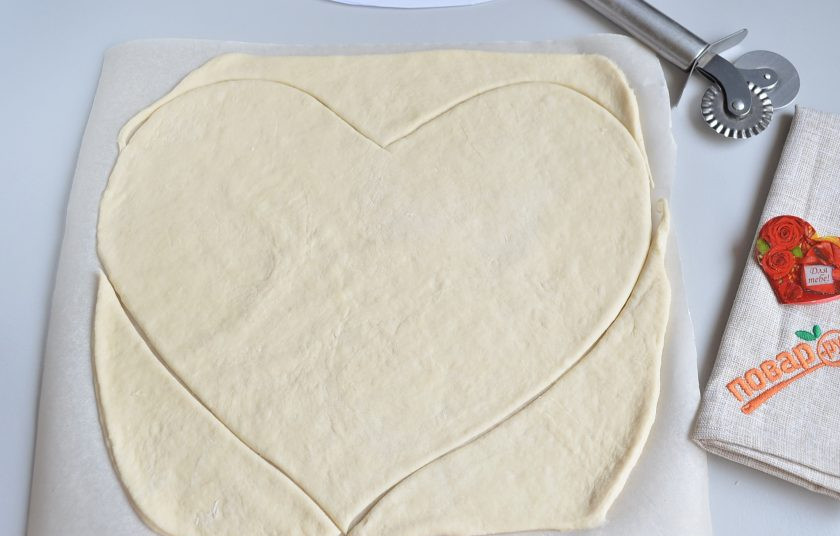 1. Этап. Пицца на 14 февраля: 4. Притрусите стол мукой, раскатайте тонко тесто. Перенесите его пергамент, вырежьте сердечко.